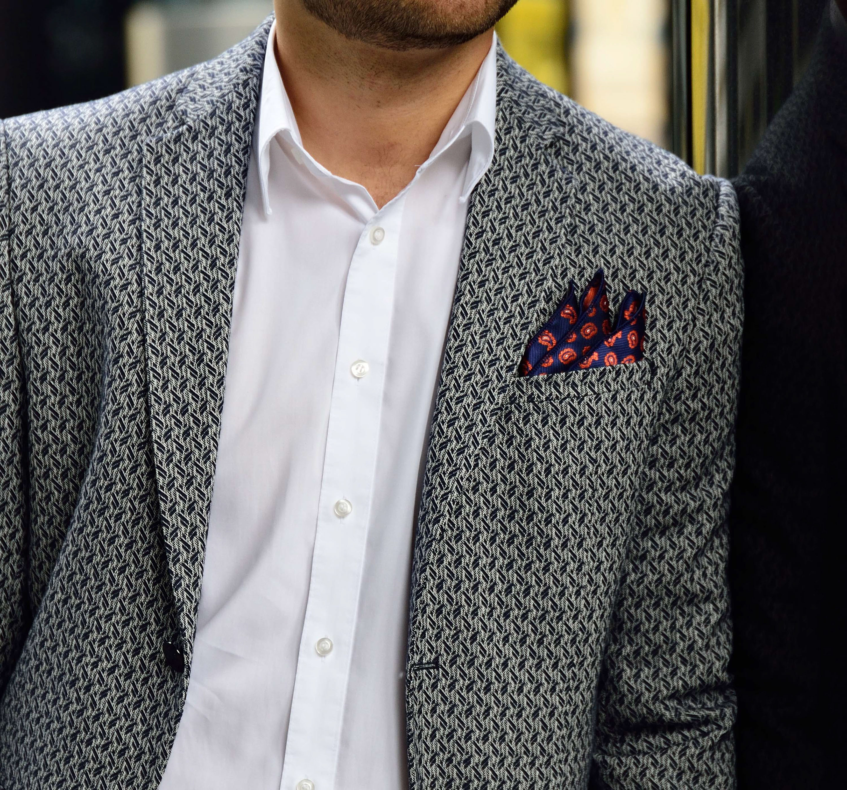 Four self-confident men wearing di Venisco pocket squares standing in front of a modern building.